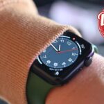 Apple Watch on a wrist wearing a brown sleeve, accompanied by a red badge indicating a daily deal offer.