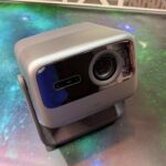 A sleek, modern projector with a lens situated on a table with a vibrant, cosmic-themed surface.