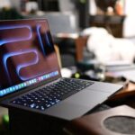 Open laptop with glowing keyboard resting on a sofa, abstract screen background, in a cozy living room setting with blurred furniture in the background.