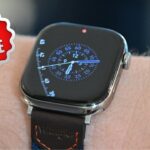 Apple Watch Series 11 on wrist displaying an analog clock face with blue numerals. Red