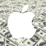 Large white apple-shaped logo centered on a background completely covered with overlapping US one hundred dollar bills.