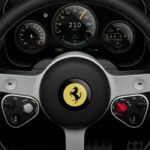 Close-up of a Ferrari steering wheel with prancing horse logo, digital speedometer reading 210 km/h, side gauges, control knobs, and paddle shifters in a modern sports car cockpit