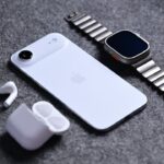 iPhone Air, Apple Watch with metal band, and AirPods with open case on gray fabric background, with a pink badge on the left reading percent sign price drop