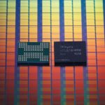 Two small SK hynix memory chips resting on a colorful, grid-patterned silicon wafer background with vertical rows in gradients of red, orange, yellow, green, and blue