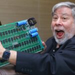 Apple founder Steve Wozniak, holding up an Apple-1 green logic board, in a crowd of people