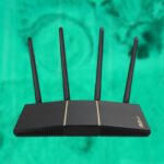 Black wireless router with four upright antennas centered against a bright teal abstract background