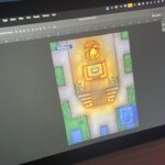 Tablet screen showing Adobe Photoshop with a colorful top-down temple map open, featuring glowing central altar, statues, surrounding greenery, pools, and a small blue floor-plan inset