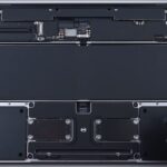 Open laptop base showing internal components, including large central battery and circuit boards, with a gloved hand on the right side preparing for repair or disassembly