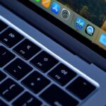 Close-up of a MacBook laptop keyboard and macOS dock on screen, with a red circular Daily Deal badge in the upper-right corner indicating a special offer or promotion